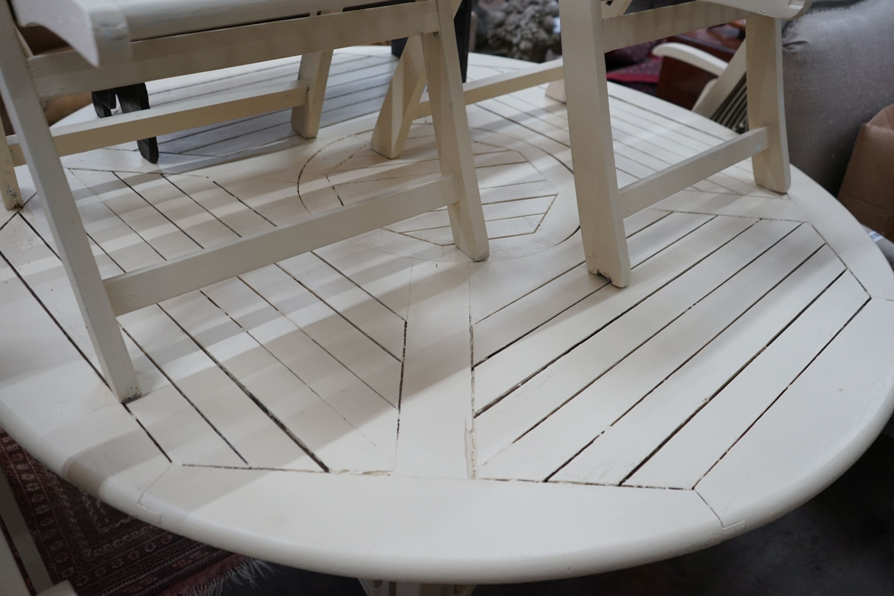 A circular painted teak garden table, diameter 150cm, height 72cm and six folding elbow chairs